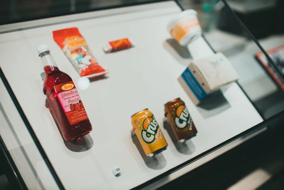 Collection of drinks and snacks showcased in a glass display case, indoors.