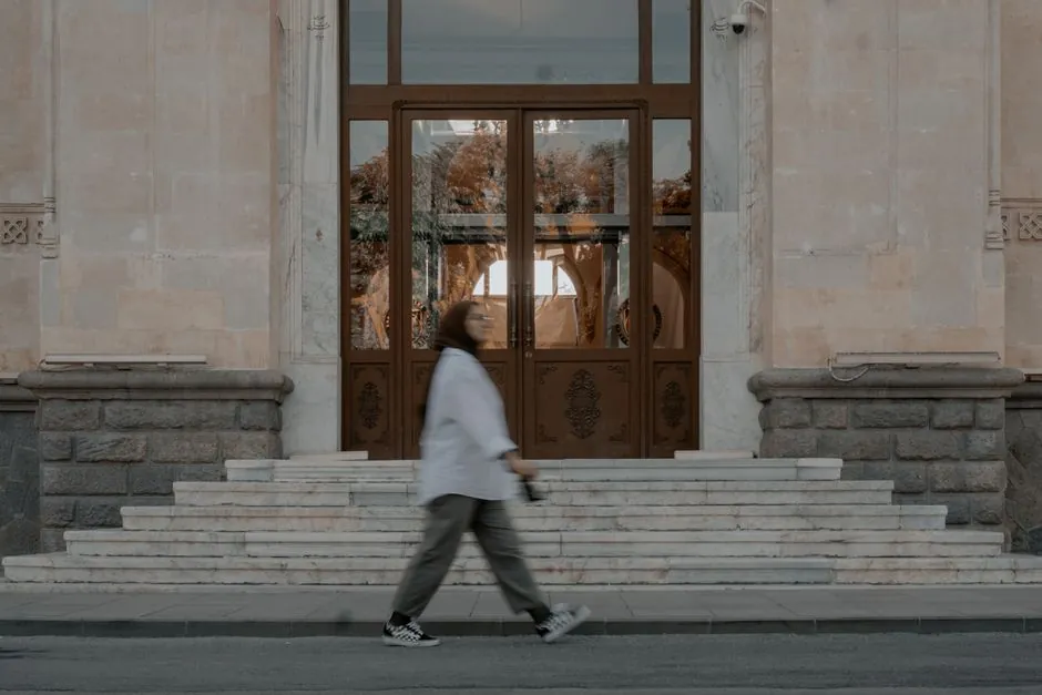 Woman in motion blur walking past a grand entrance with intricate glass doors.