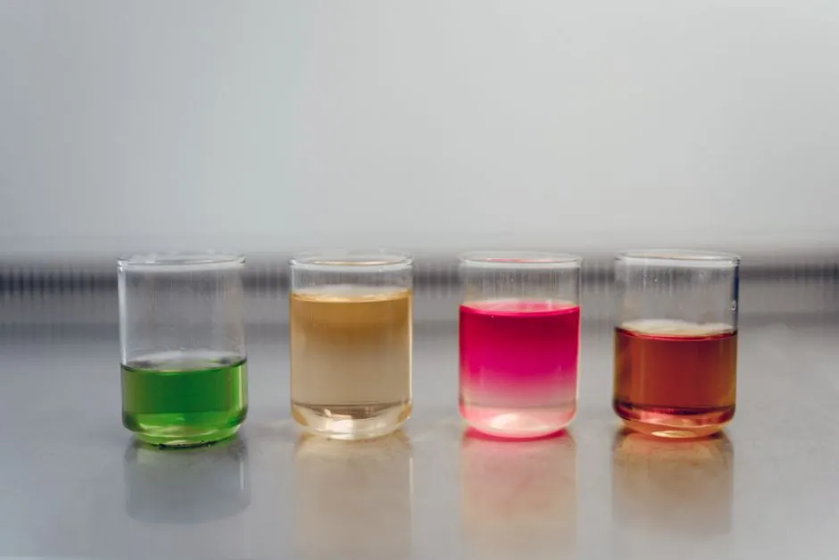 Four glasses filled with colorful liquids on a laboratory table, showcasing a chemical experiment.
