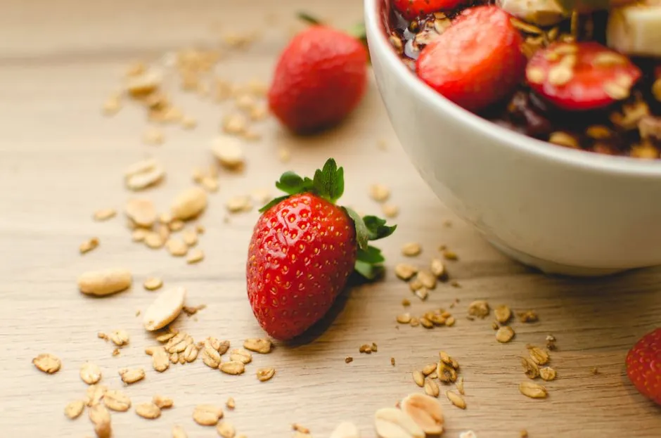 A close-up of a fresh strawberry breakfast bowl with granola on a wooden table, highlighting health and nutrition.
