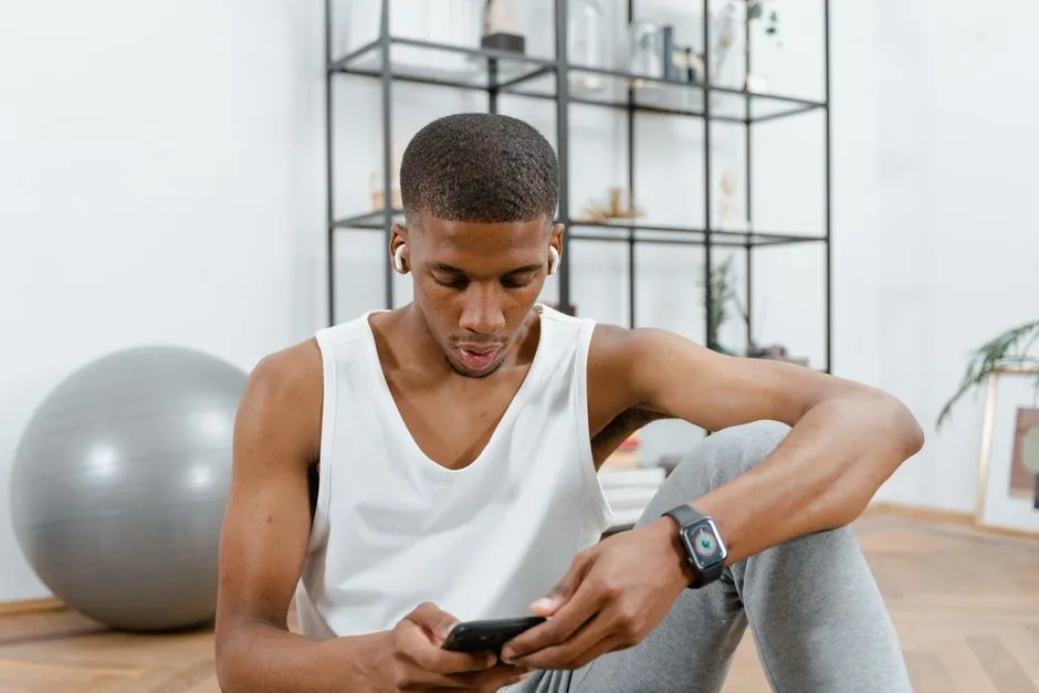 Young man in casual wear, sitting indoors, engaging with smartphone.