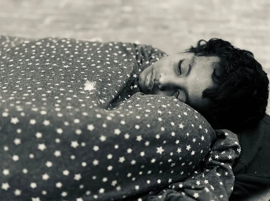A child with black hair sleeps peacefully in a star-patterned blanket indoors.