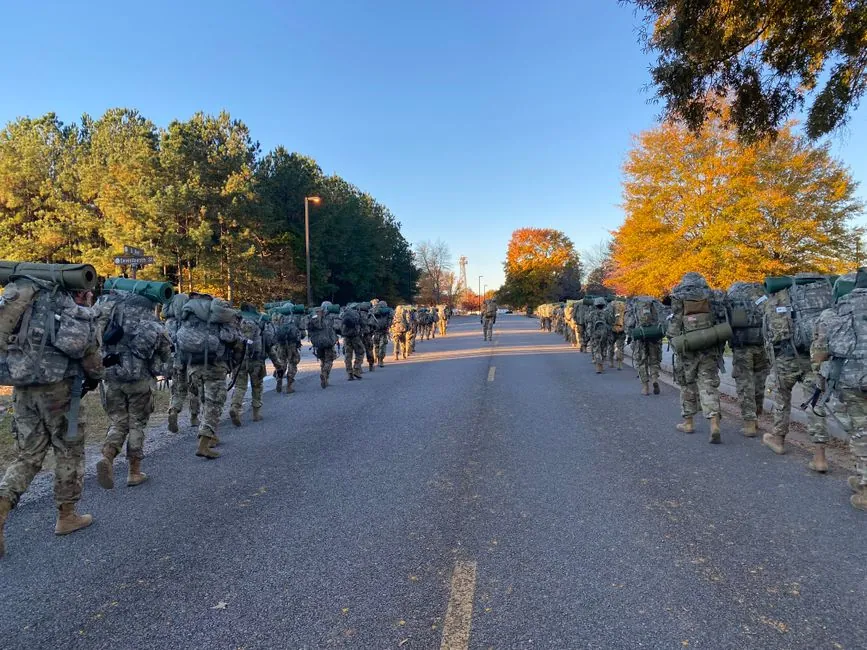 Soldiers in camouflage uniforms marching down a forest road during autumn.