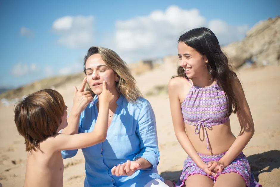 A mother with her kids applying sunscreen on a sunny beach in Portugal.
