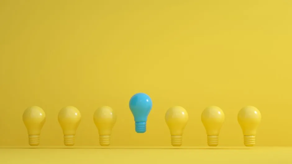 A standout blue light bulb among several yellow bulbs on a yellow background, symbolizing innovation.