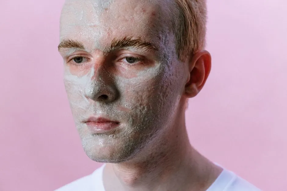 Portrait of a young man with a clay face mask against a pink background, highlighting skincare and beauty routines.