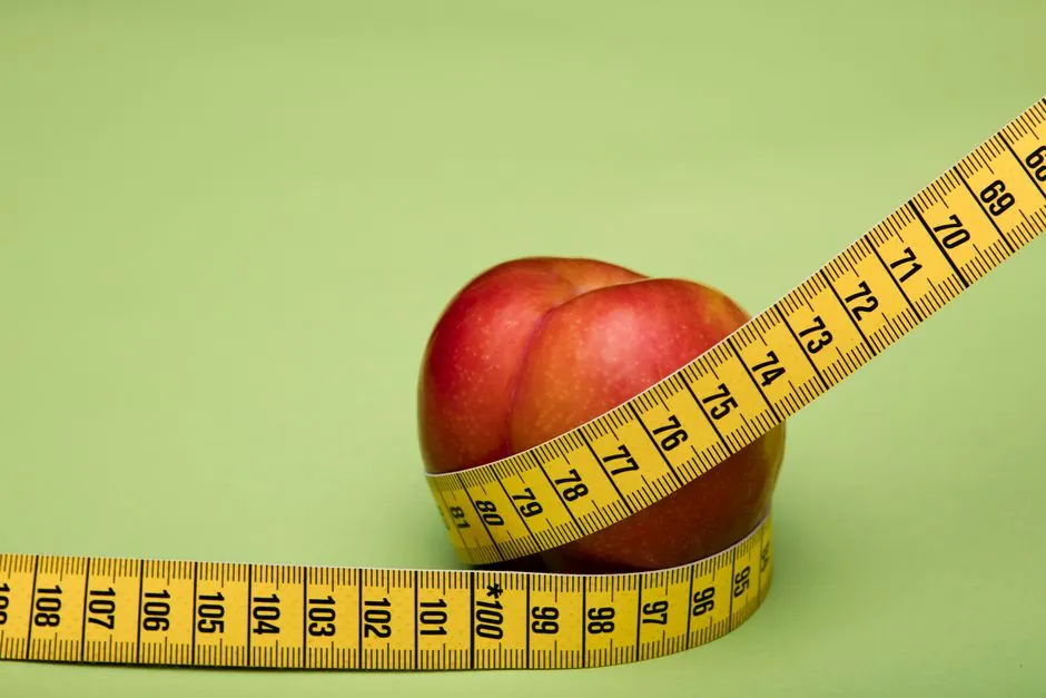 Red apple wrapped in a yellow measuring tape against a green backdrop emphasizes freshness and health.
