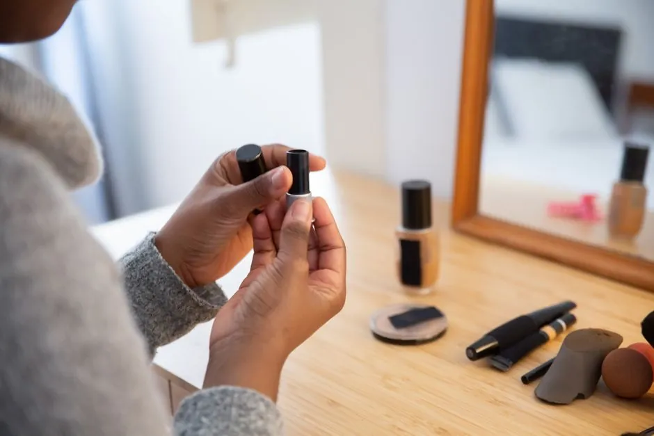 Woman's hands holding lipstick at vanity desk with makeup tools, reflecting casual routine.