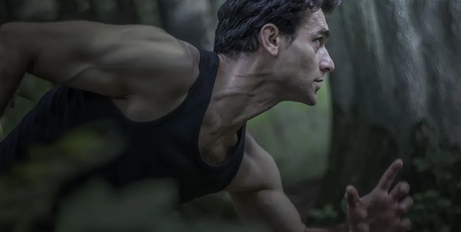 A focused athlete in motion running through a dense forest.