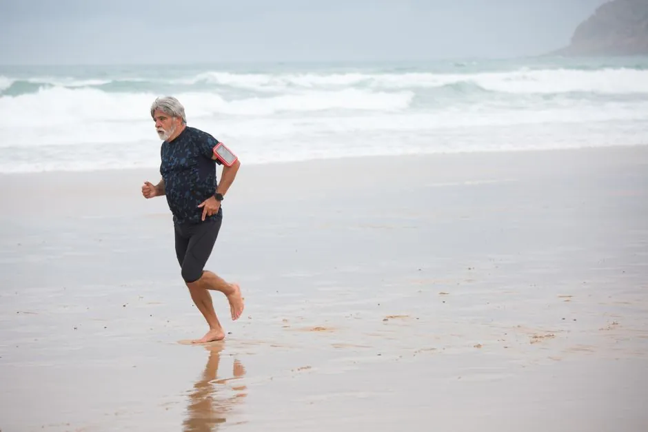 Elderly man jogging barefoot on a Portuguese beach, embracing a healthy lifestyle.