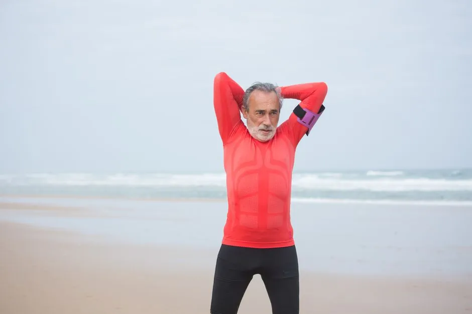 Elderly man in red sportswear stretching on a serene Portuguese beach.