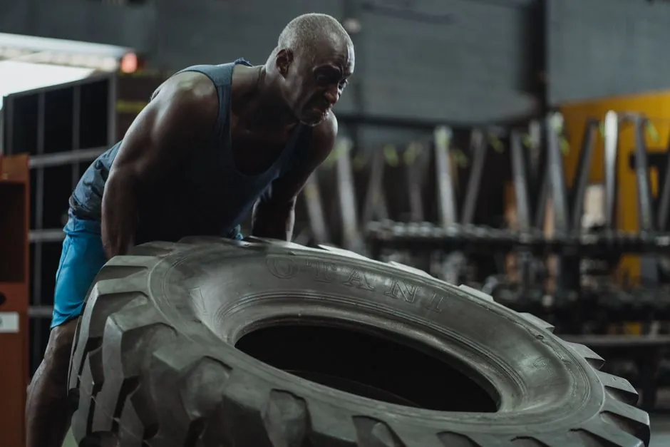 Muscular man performing tire flip exercise in a gym, showcasing strength and determination.