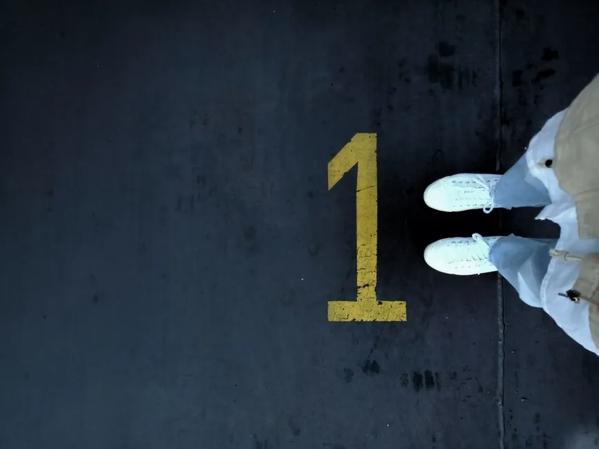 Aerial shot of white sneakers on a dark surface with a painted yellow number one.