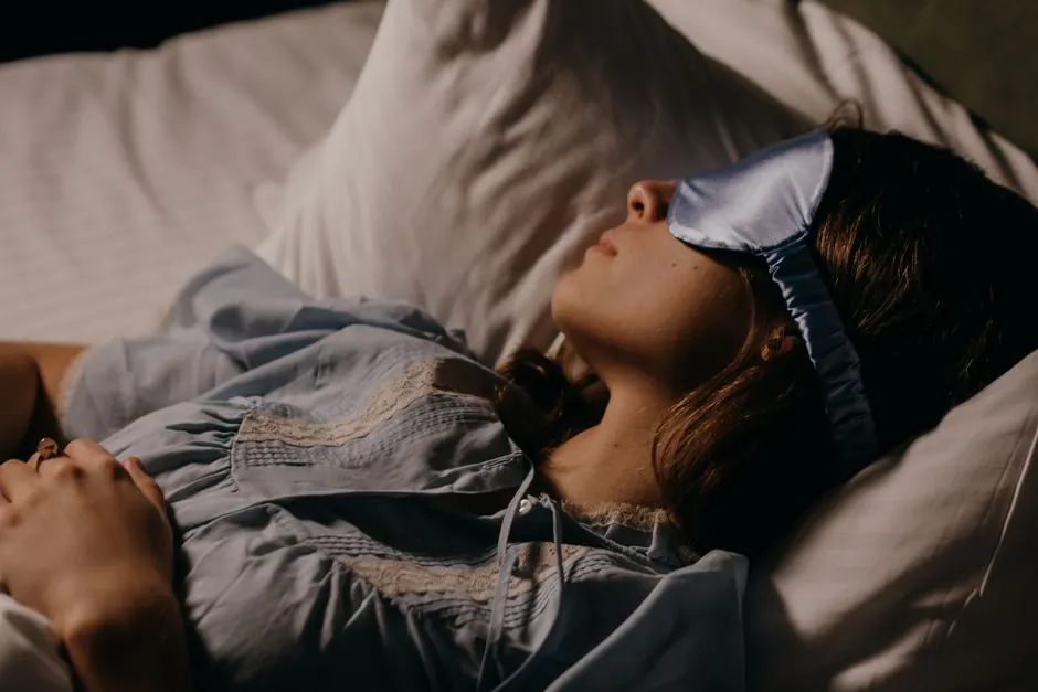 A woman peacefully sleeping with a blue eye mask in a dimly lit room.