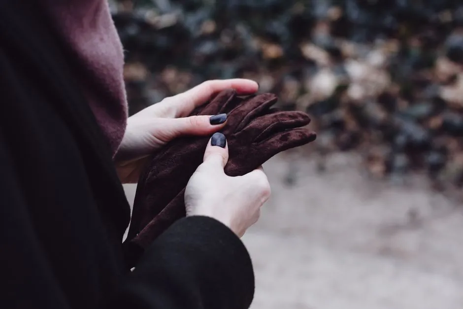 Close-up of a woman adjusting her warm brown gloves outdoors, capturing winter vibes.