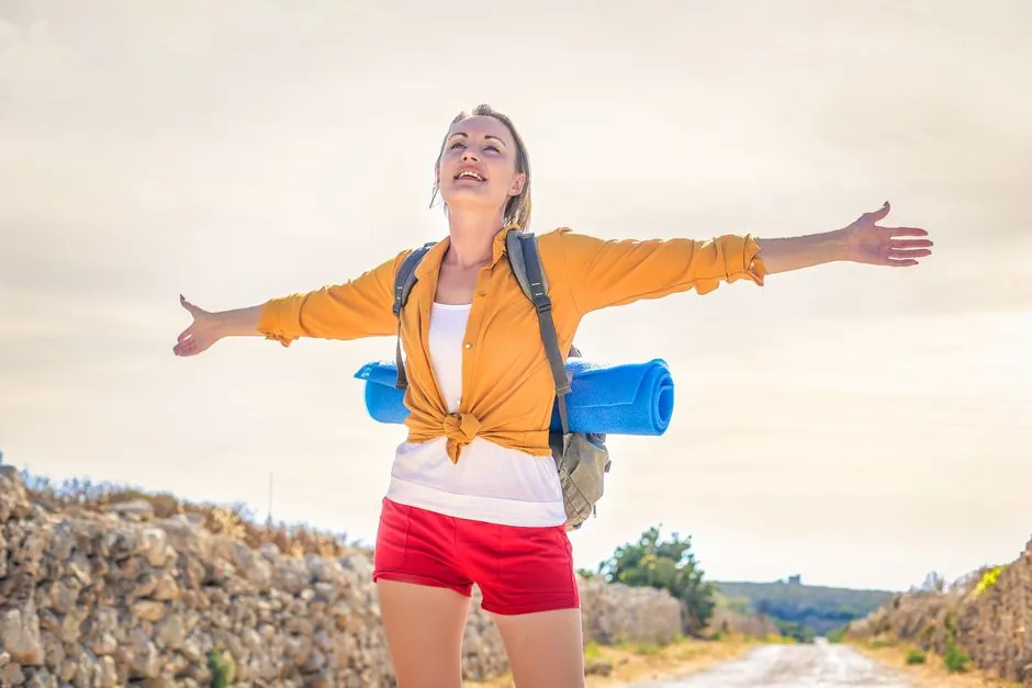 Happy woman basking in sunlight on a summer hike with yoga mat.