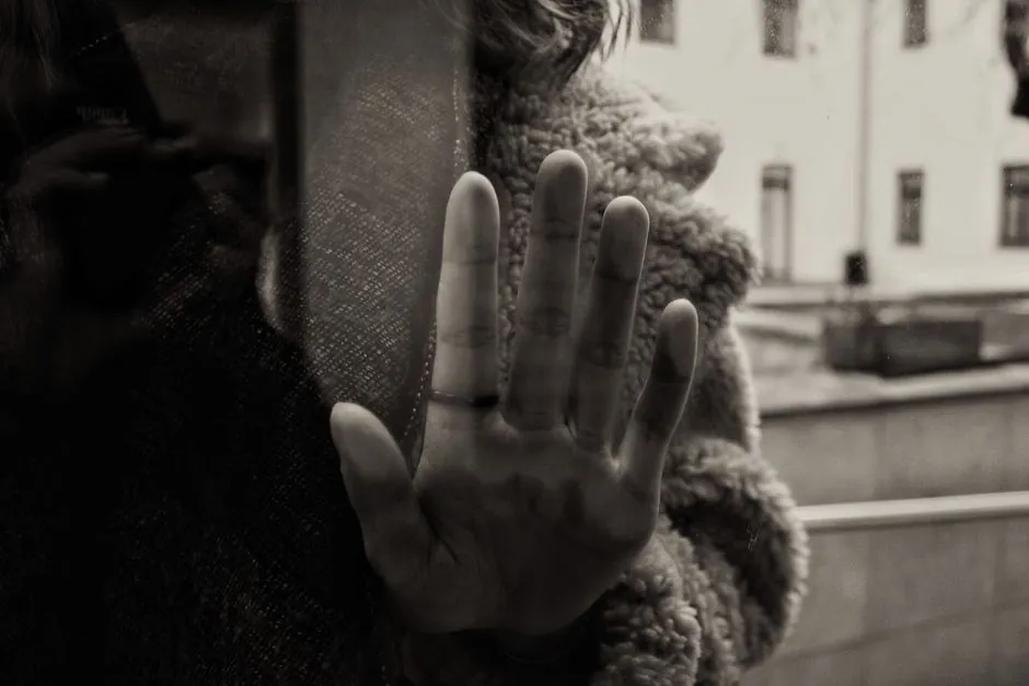 A moody black and white photo of a hand touching glass with a reflection.