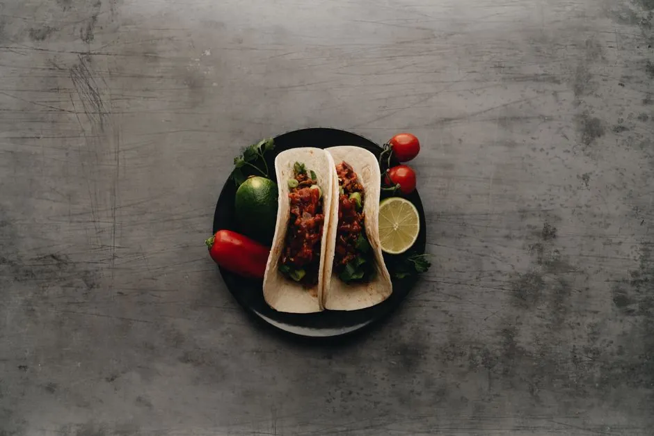 Delicious tacos with fresh cherry tomatoes, lime, and pepper on a plate, perfect for a Mexican-themed meal.