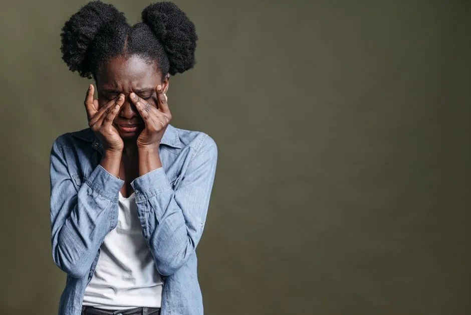 A woman expresses deep emotion with her eyes closed, hands on face, against a green backdrop.