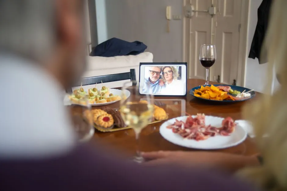 Couple dining with assorted appetizers and wine, chatting via video call on a tablet.